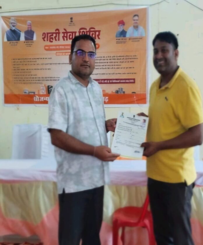 लाभार्थी उदय सिंह गुर्जर को मकान का पट्टा प्रदान करते अधिकारी